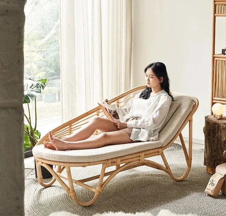 A person relaxing in a natural rattan woven chaise lazy chair, reading a book.