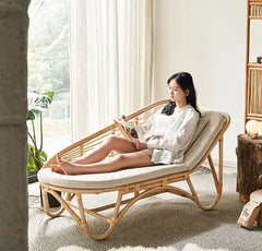 A person relaxing in a natural rattan woven chaise lazy chair, reading a book.