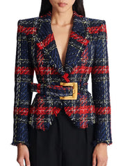 Model wearing a navy and red plaid tweed blazer with a wide belt and gold buckle, styled over black trousers on a studio backdrop