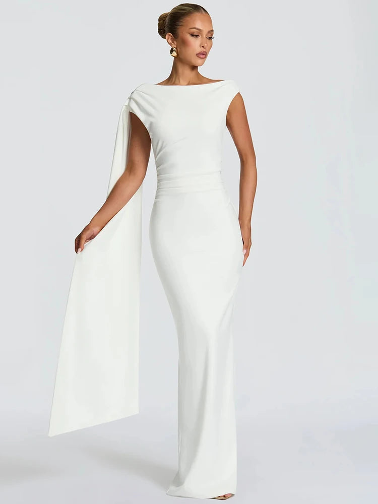 Off-shoulder maxi dress with a long draped panel flowing from one side, captured in a clean studio setting with graceful movement.