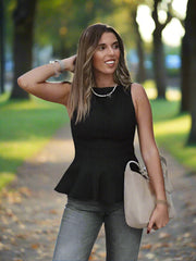 Woman wearing a peplum top styled for office-to-dinner outfits and gray pants, holding a beige handbag.