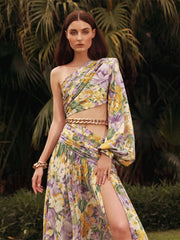 A model wearing a floral printed one-shoulder chain maxi dress with gold-tone chain detail and a side hollow detail.