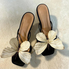 Black sandals with large white butterfly decorations on a light background