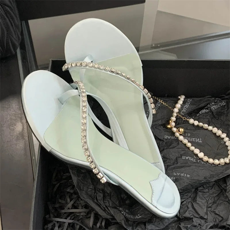 Light blue sandals with rhinestone straps on a black surface