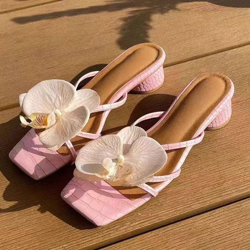 Pink high-heeled shoes with white orchids on a wooden surface