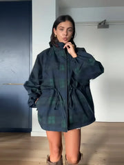 Model wearing a dark plaid hooded jacket zipped up, showing the oversized fit and relaxed shape in a clean indoor setting.