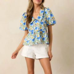 Woman wearing a pastel print top with a scalloped collar and ruffled hem, and white shorts against a beige background
