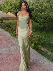 Woman in a light green evening gown standing outdoors on a paved path with greenery.
