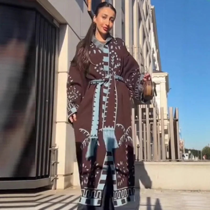 Outfit shot featuring a brown patterned longline cardigan paired with jeans and a blue structured handbag in a minimalist indoor setting.