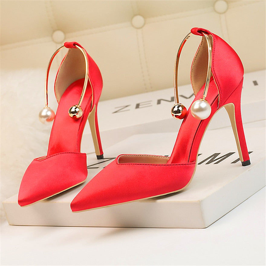 A pair of red high heels with pearl metal buckles and open-toe platforms, displayed on a bubble bag outsole.