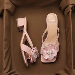 Pink square heel sandals with pearl flower accent, styled for summer events  on a brown fabric background