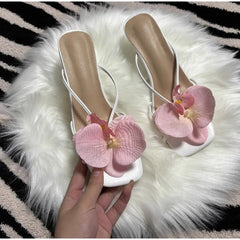Beige high-heeled shoes with pink floral decorations on a fluffy white surface.