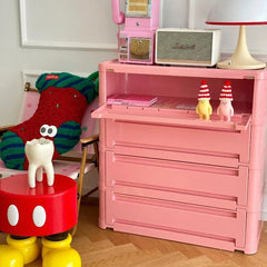 “Pink plastic nightstand with drawer and open shelf in bedroom setting”