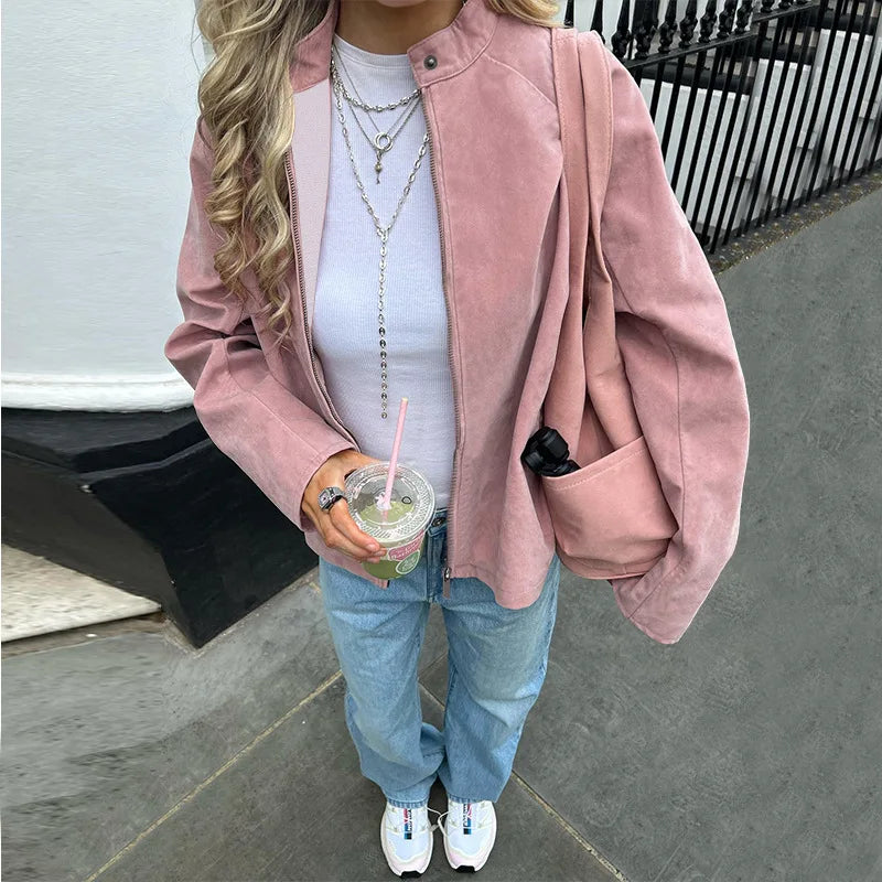 Person wearing a pink suede zip mock neck jacket styled for casual layering in autumn with a white shirt and blue jeans, holding a drink.