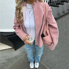 Person wearing a pink suede zip mock neck jacket styled for casual layering in autumn with a white shirt and blue jeans, holding a drink.