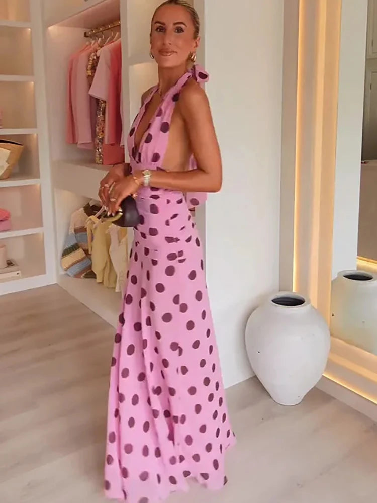 Woman in a pink polka dot dress standing in a room with shelves and decor.
