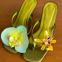 Green high-heeled sandals with floral decorations on a wooden surface