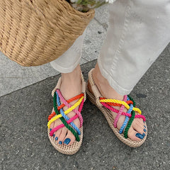 Colorful woven sandals with a straw sole worn by a person on a pavement.