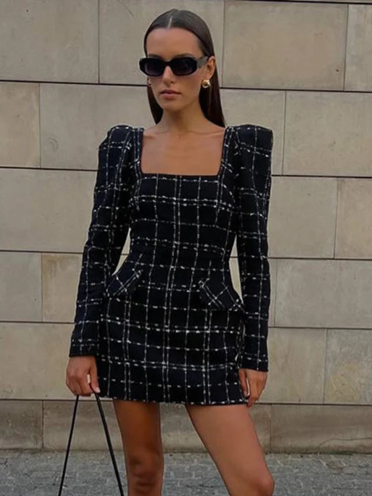 Woman wearing a black and white checkered dress against a stone wall.