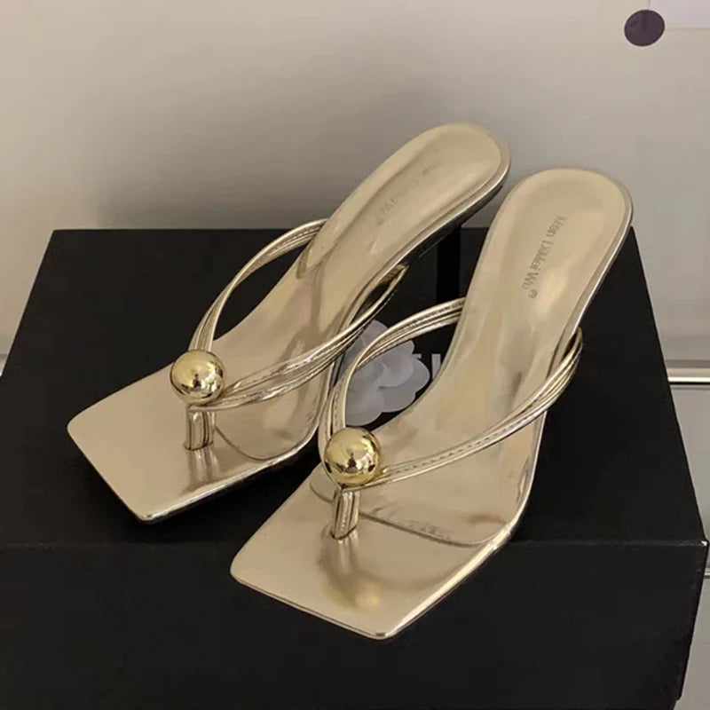 Gold high-heeled sandals with spherical embellishments on a black surface.