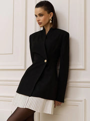 Asymmetric blazer-style mini dress with a sculpted neckline and pleated hem shown in a warm interior setting for a polished city look.