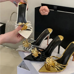 Black high-heeled shoes with gold embellishments on a white surface.
