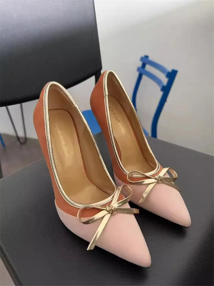 Pair of high-heeled shoes with gold bows on a dark surface.
