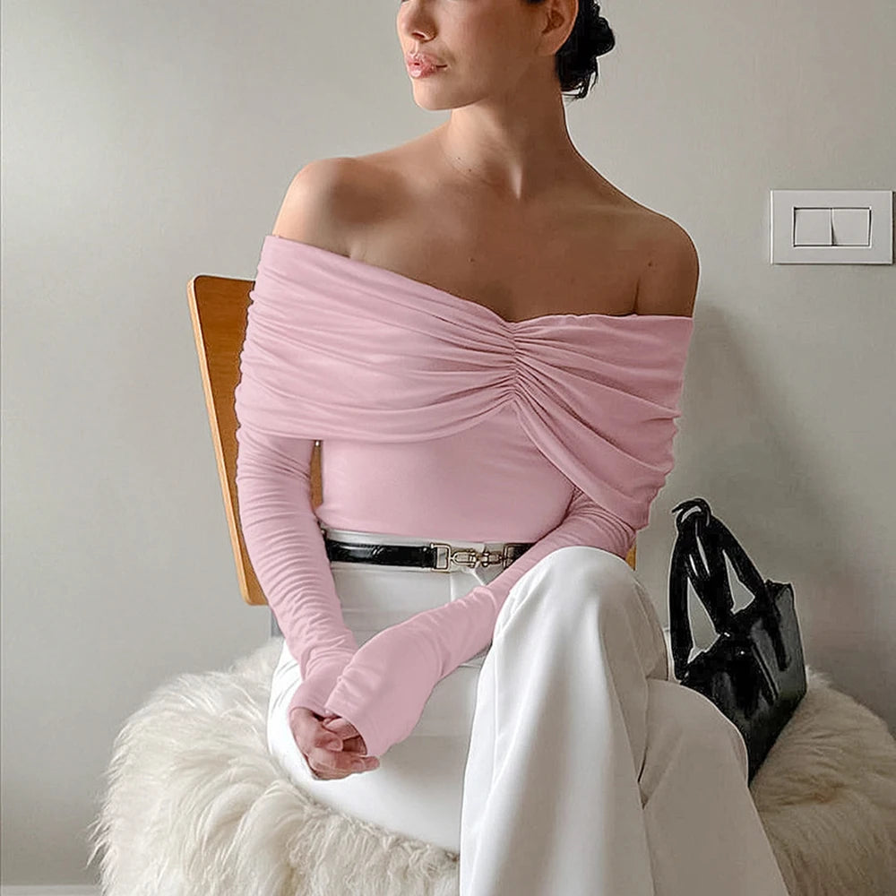 Woman wearing a pink off-shoulder top and white pants sitting on a chair.
