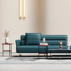 A green, modular, curved leather sofa set with a solid wood frame, placed in a minimalist decor setting with a white wall and simple decorative items around.