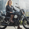 A Woman Biker in her Motor Bike  wearing a Women’s block heel mid-calf boots with decorative metal buckles worn by a person sitting on a wooden floor.