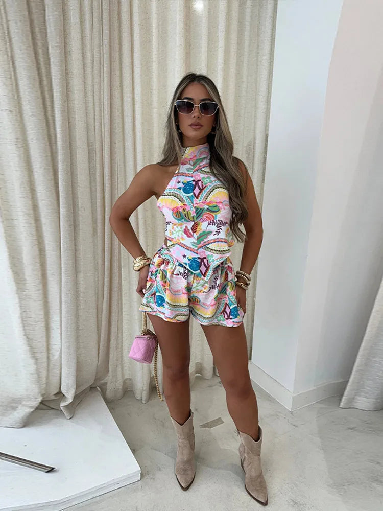 A woman wearing a printed halter-neck top and matching shorts, indoors with sunglasses and a pink handbag.