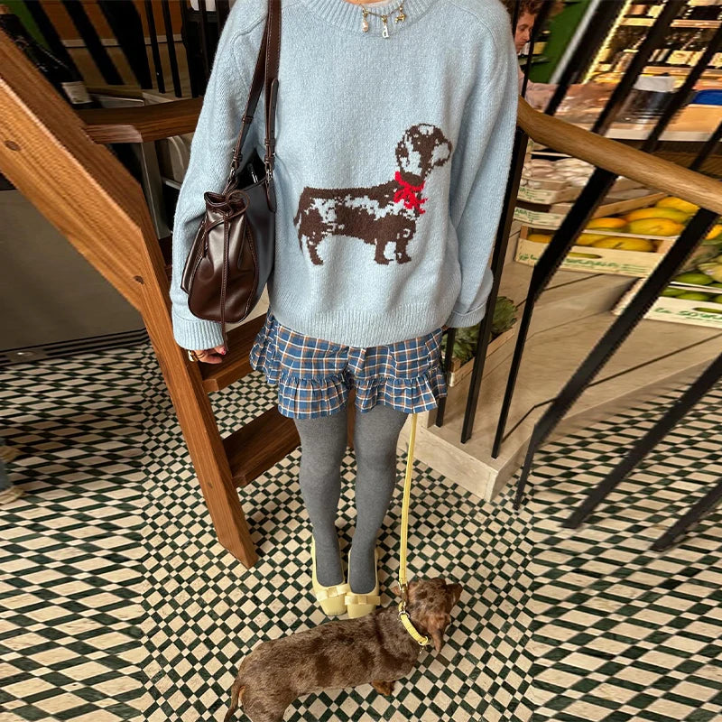 Person wearing a sweater with a dog design, holding a brown bag, and standing on a checkered floor.