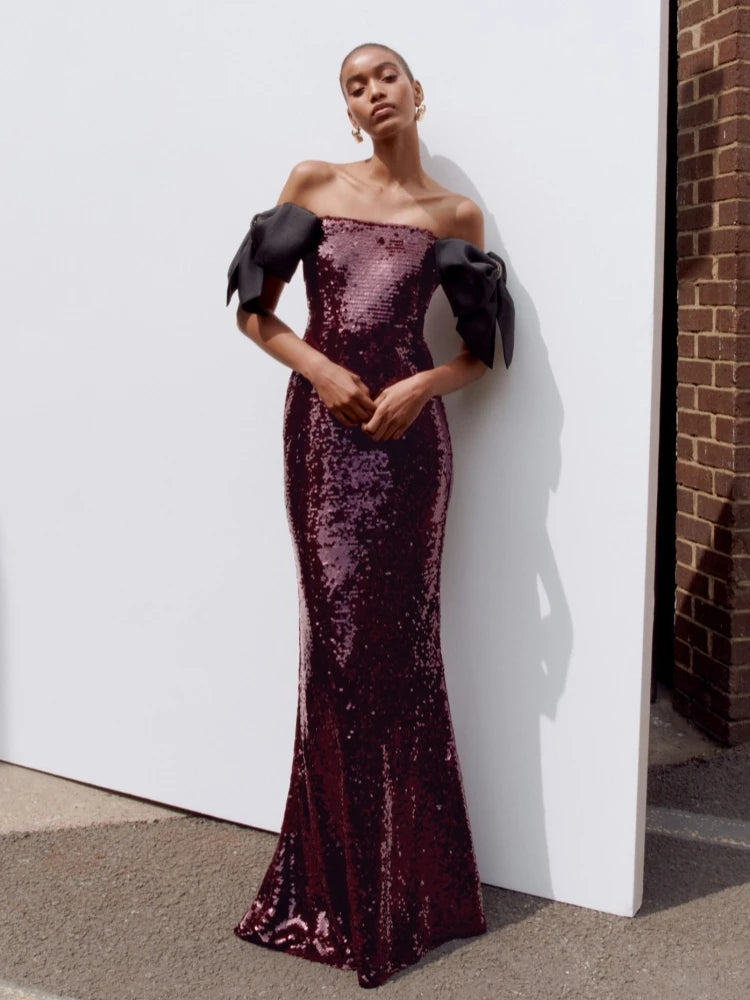 Full-length view highlights the strapless neckline, fitted torso, and ankle-length hem on a purple sequin gown with contrast bow sleeves.