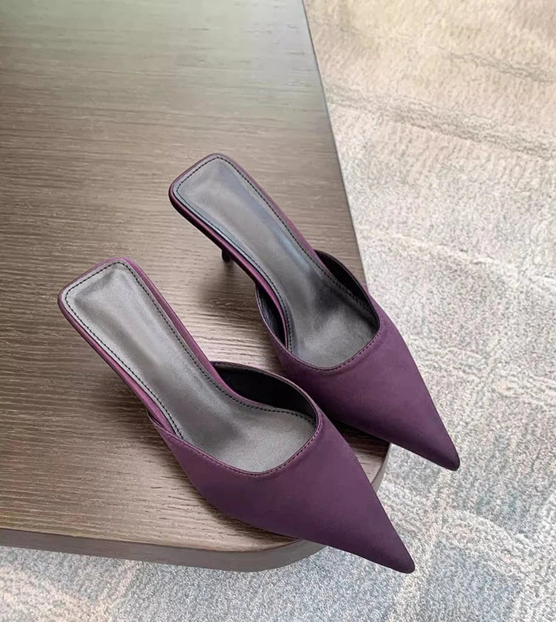 Purple pointed toe high heel mules placed on wooden table