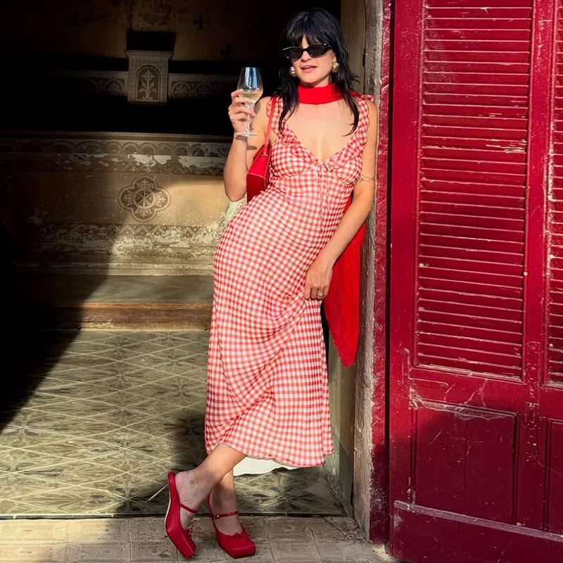 Woman in a red gingham maxi dress styled for a picnic-to-party summer look holding a glass of wine, standing in front of a red door.