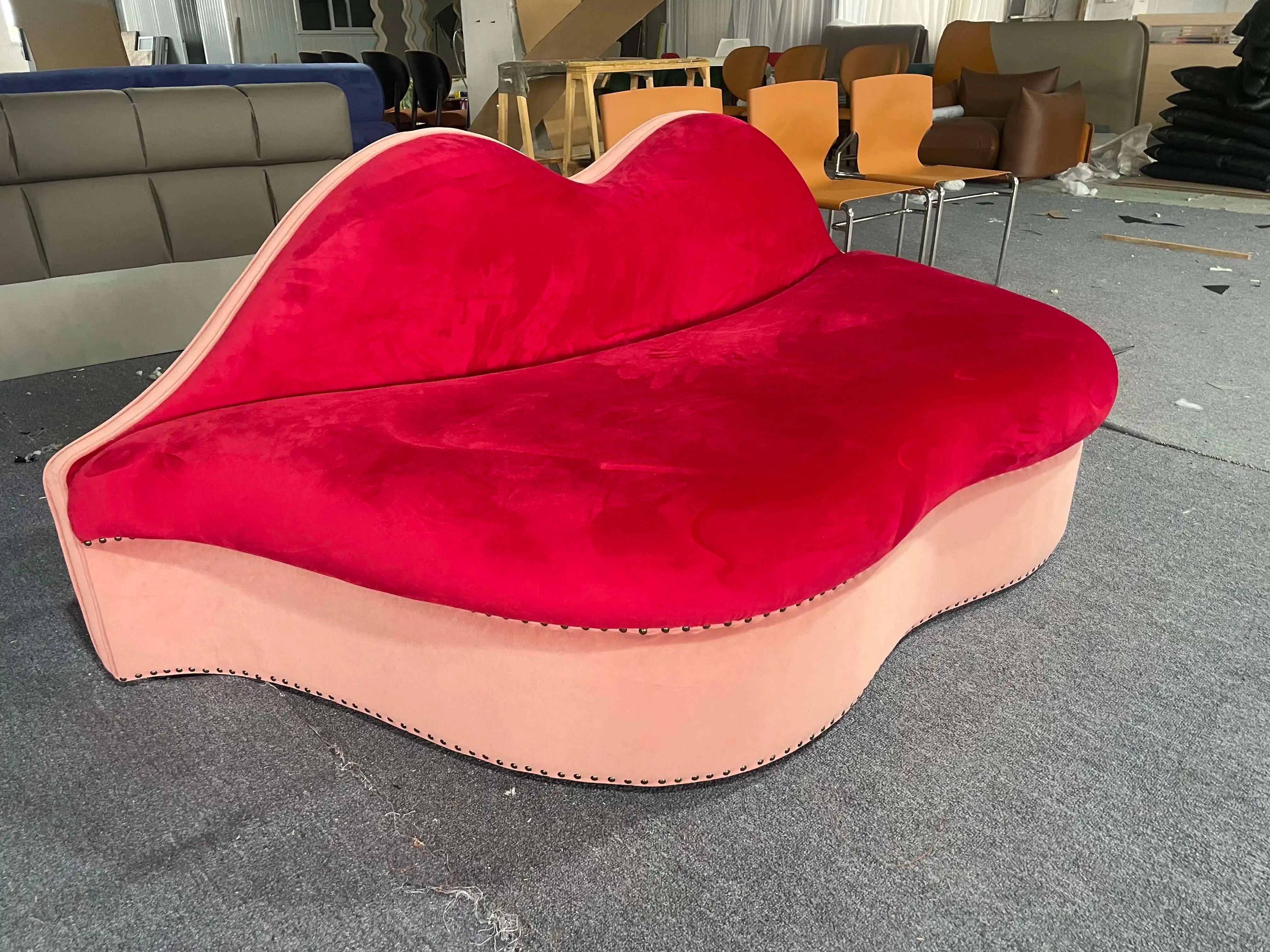 A red lip-shaped velvet fabric loveseat sofa displayed in a showroom setting.