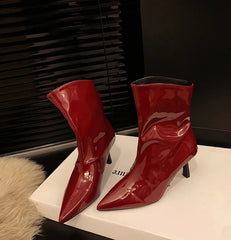 Pair of red patent leather ankle boots on a white surface with a dark background
