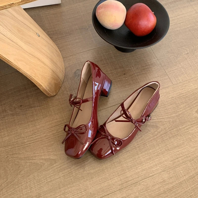 Shiny red Mary Jane shoes with bow detail on wooden surface