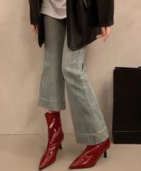 Person wearing red patent leather boots with light blue jeans against a neutral background