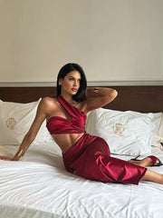  Woman wearing red satin one-shoulder cutout bodycon dress sitting on bed  with white pillows and a wooden headboard.
