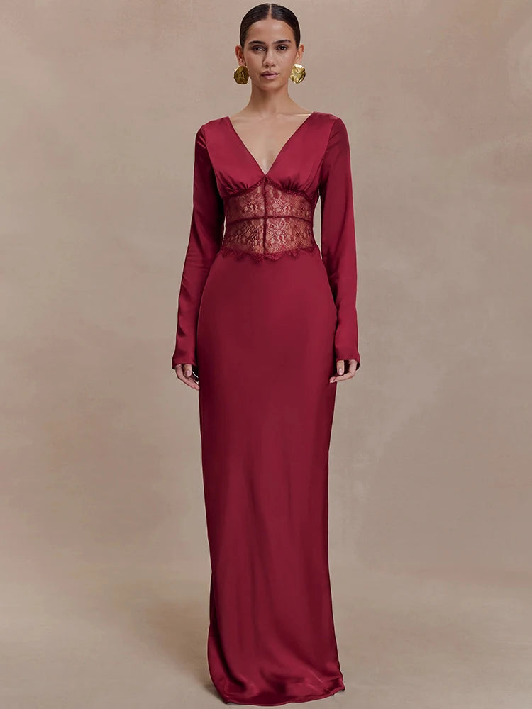 Model wearing a red long sleeve maxi dress with a deep V neckline and sheer lace waist panel against a warm beige studio backdrop.