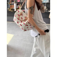 Person holding a Handbag worn on the shoulder, styled with a casual white outfit  in an indoor setting