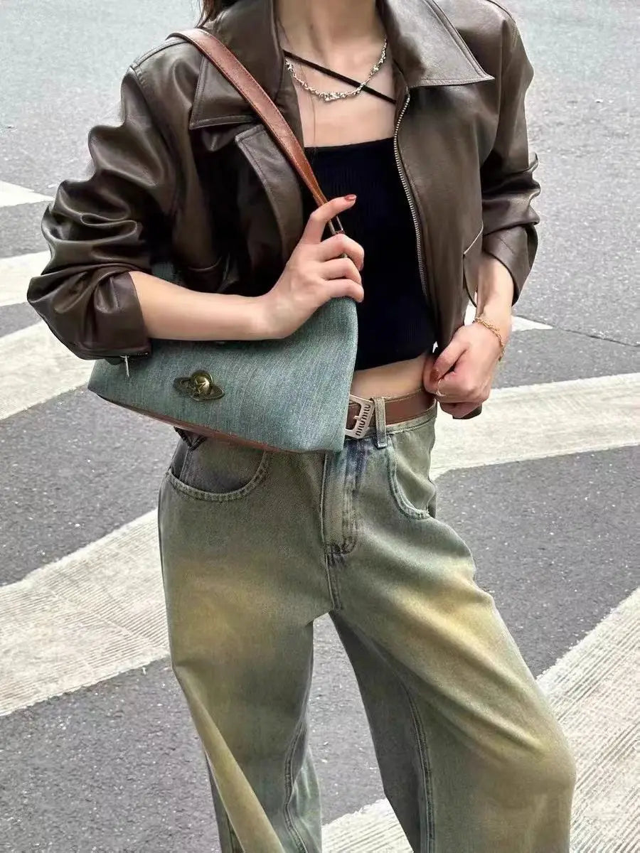 A person wearing a vintage denim hobo bag with a brown strap styled for casual wear, holding a blue handbag on a street.