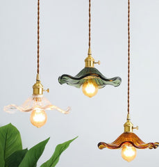 Three pendant LED lights with colourful glass shades in blue, champagne,  red, ink green, as flowers with polished copper finishes, and hanging from the ceiling light blue back ground  and green leaf.