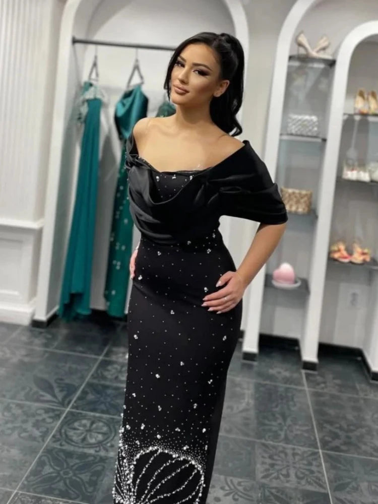 Woman wearing a rhinestone beaded black evening dress with floor length silhouette in a store setting.