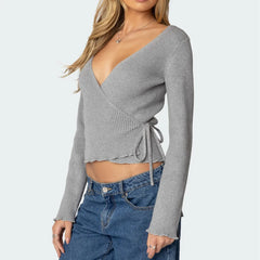 A woman wearing a grey ribbed knit sweater and blue jeans on a white background.