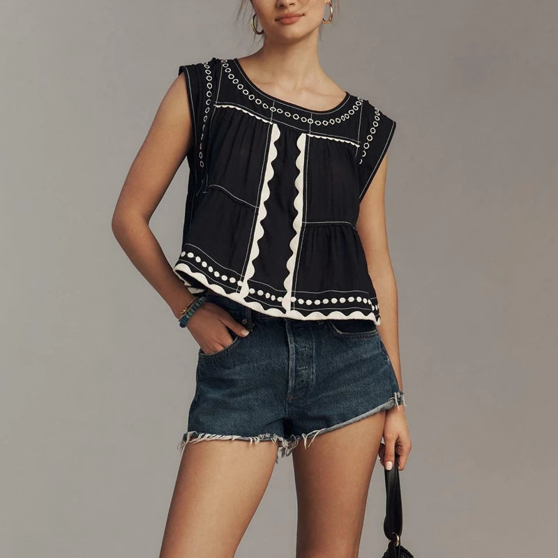 Woman wearing a  ric-rac-trim-embroidered-crop-top-black with denim shorts on a grey background