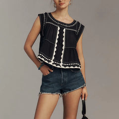 Woman wearing a  ric-rac-trim-embroidered-crop-top-black with denim shorts on a grey background