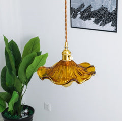 A pendant LED lights with colourful glass shades in brown, as flowers with polished copper finishes, and hanging from the ceiling, light blue background with a painting and green leaf pot.