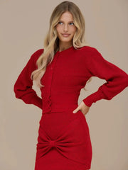 Close-up of the round neckline and button placket on the red knit top, showing the textured knit finish and clean tailoring.